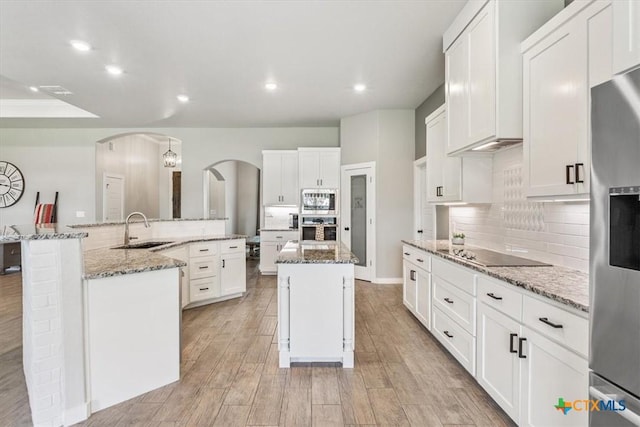 100 Metheglin Dr, Temple, TX 76502 - kitchen featuring appliances with stainless steel finishes, a large island with sink, arched walkways, decorative backsplash, and white cabinetry