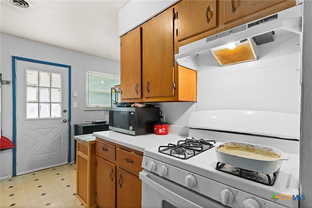 603 S 13th St, Copperas Cove, TX 76522 - kitchen featuring white range with gas cooktop, under cabinet range hood, stainless steel microwave, light countertops, and brown cabinets