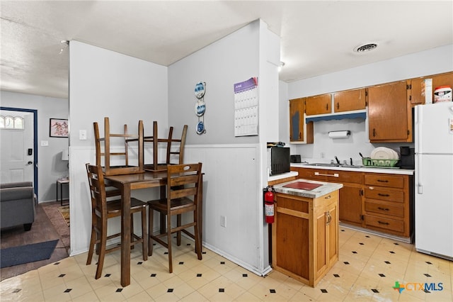 603 S 13th St, Copperas Cove, TX 76522 - kitchen featuring freestanding refrigerator, brown cabinetry, wainscoting, and light countertops