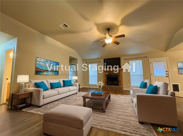 living area with visible vents, ceiling fan, wood finished floors, vaulted ceiling, and a fireplace