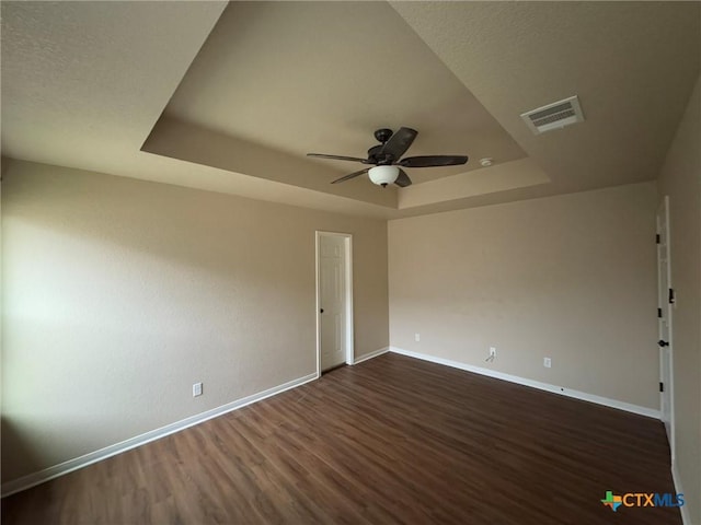 spare room with a tray ceiling, ceiling fan, and dark wood-type flooring