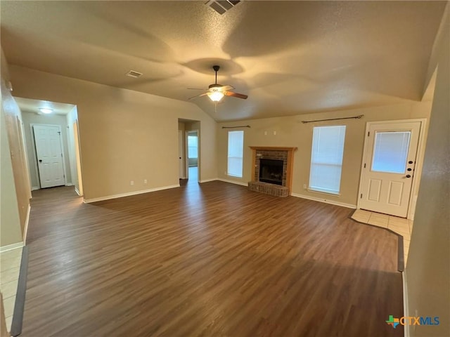 unfurnished living room featuring lofted ceiling, a brick fireplace, ceiling fan, dark hardwood / wood-style floors, and a textured ceiling