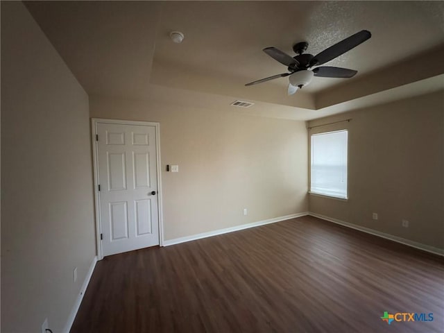 spare room featuring ceiling fan, dark hardwood / wood-style flooring, and a tray ceiling