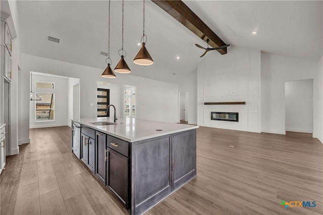 kitchen featuring sink, pendant lighting, a fireplace, a center island with sink, and light wood-type flooring