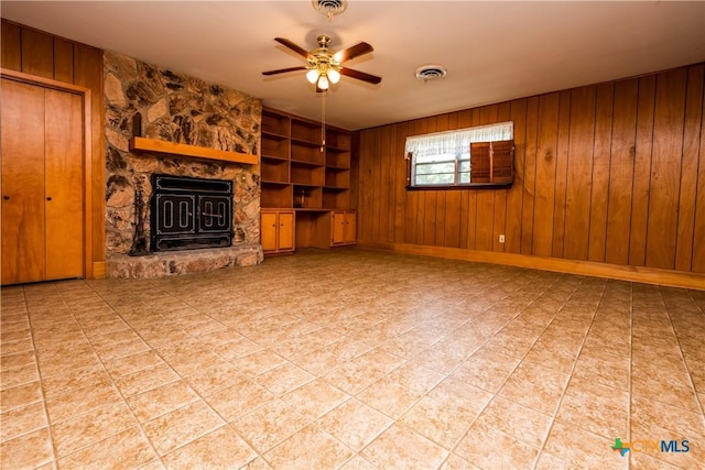 unfurnished living room featuring built in shelves, ceiling fan, a fireplace, and wooden walls