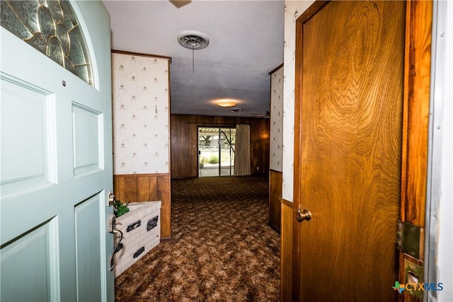 hall featuring dark colored carpet, a textured ceiling, and wooden walls