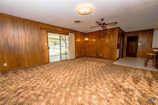 unfurnished living room with light colored carpet, ceiling fan, and wooden walls