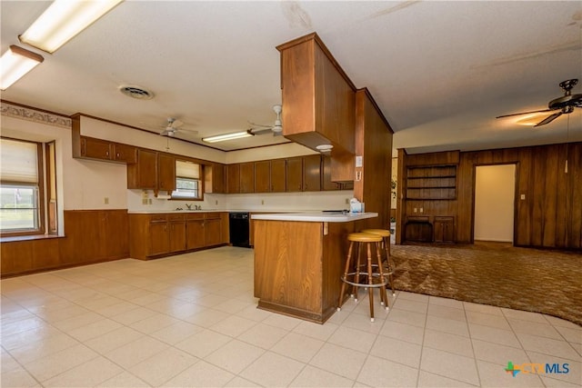 kitchen with ceiling fan, sink, kitchen peninsula, wood walls, and a breakfast bar