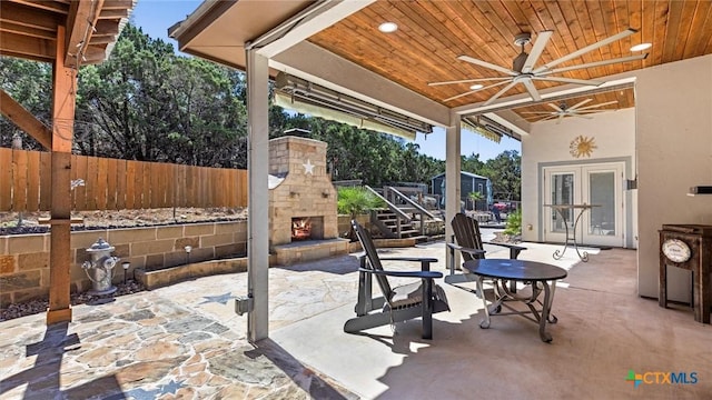 view of patio featuring an outdoor stone fireplace, a ceiling fan, and fence