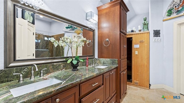 bathroom featuring a shower stall, double vanity, baseboards, and a sink