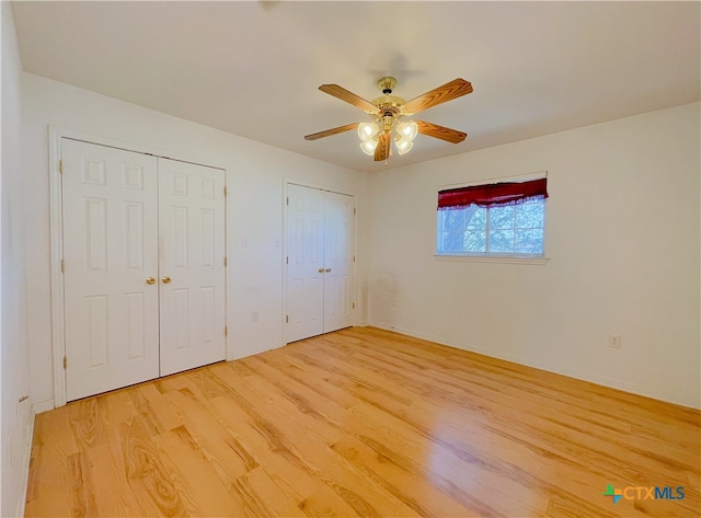 unfurnished bedroom with ceiling fan, wood-type flooring, and two closets