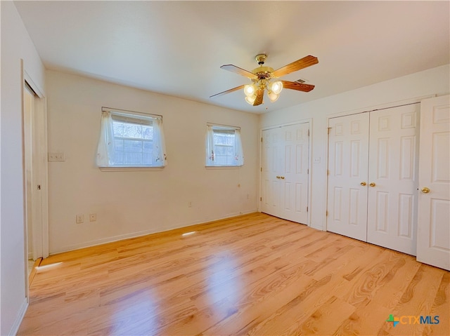 unfurnished bedroom featuring multiple closets, light hardwood / wood-style floors, and ceiling fan