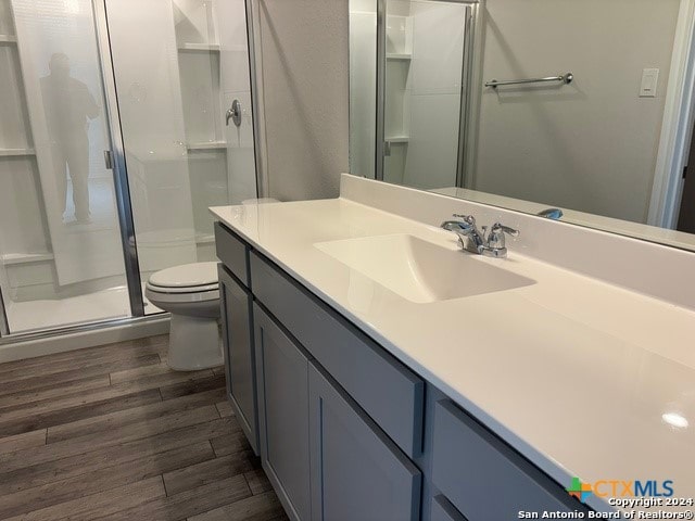 bathroom with toilet, vanity, hardwood / wood-style flooring, and a shower with door