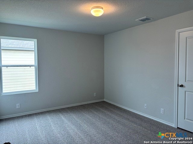 unfurnished room featuring a textured ceiling and dark carpet