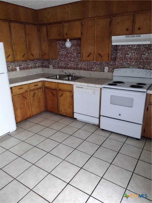 kitchen with light tile patterned flooring, white appliances, tasteful backsplash, and sink