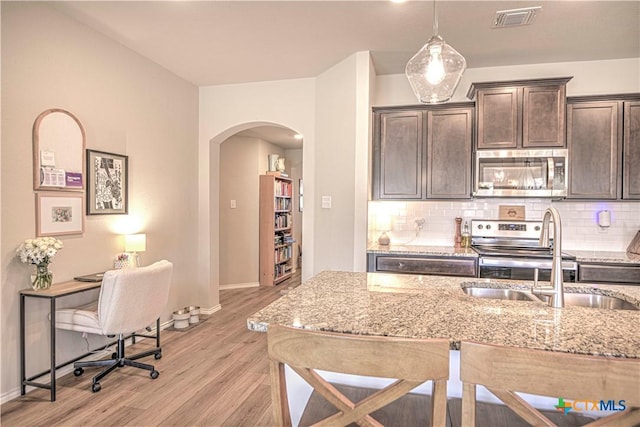 kitchen featuring visible vents, dark brown cabinets, appliances with stainless steel finishes, arched walkways, and a sink