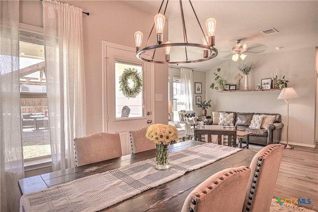 dining area featuring wood finished floors, visible vents, baseboards, vaulted ceiling, and ceiling fan with notable chandelier