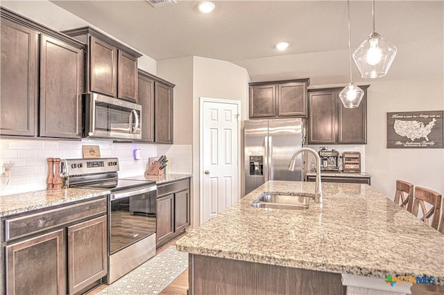 kitchen featuring dark brown cabinetry, light stone countertops, appliances with stainless steel finishes, and a sink