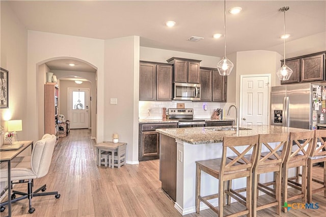 kitchen featuring dark brown cabinetry, a breakfast bar, arched walkways, stainless steel appliances, and a sink