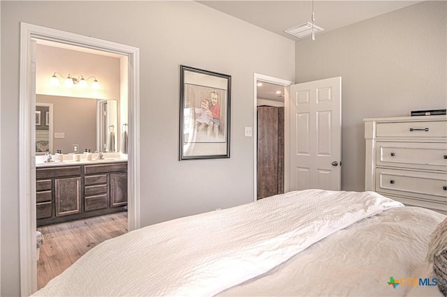 bedroom with visible vents, light wood-type flooring, ensuite bathroom, and a sink