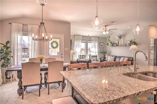 kitchen featuring hanging light fixtures, visible vents, light stone countertops, and a sink