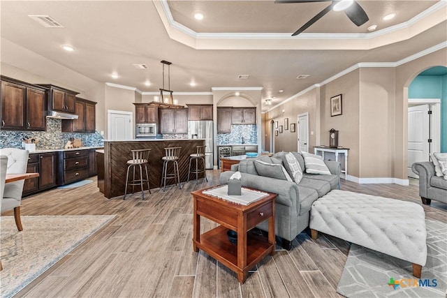 living room with a raised ceiling, ornamental molding, and light wood-type flooring