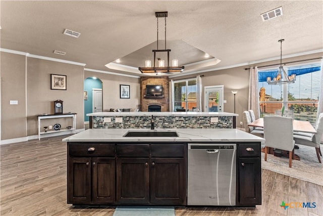 kitchen with a raised ceiling, sink, a notable chandelier, dishwasher, and hanging light fixtures