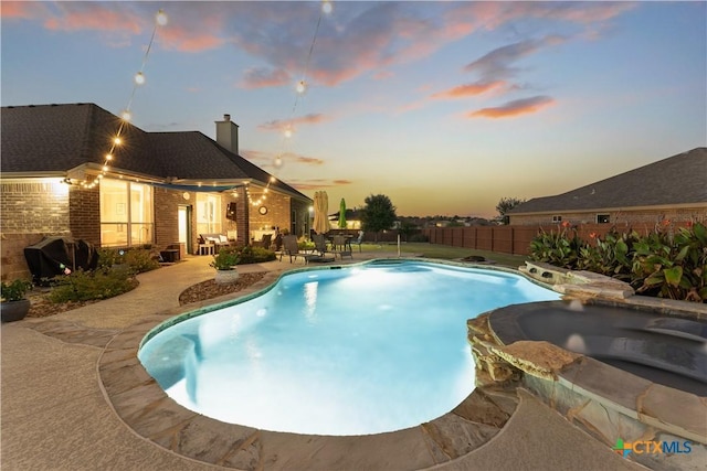 pool at dusk featuring an in ground hot tub, a patio, and area for grilling