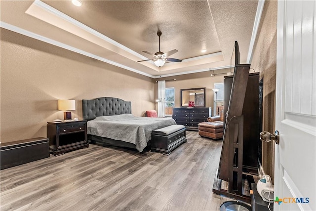 bedroom featuring ceiling fan, ornamental molding, a textured ceiling, a tray ceiling, and light hardwood / wood-style floors