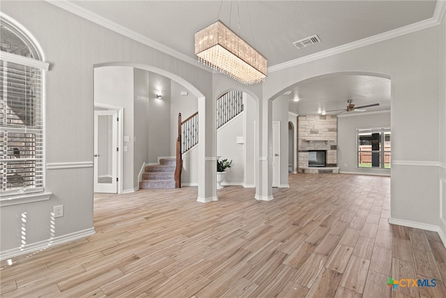 entrance foyer featuring ornamental molding, light hardwood / wood-style flooring, ceiling fan, and a stone fireplace