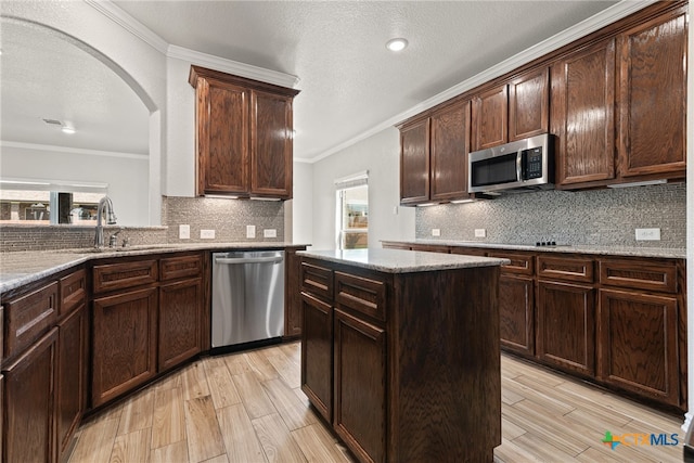 kitchen with stainless steel appliances, sink, ornamental molding, a center island, and decorative backsplash