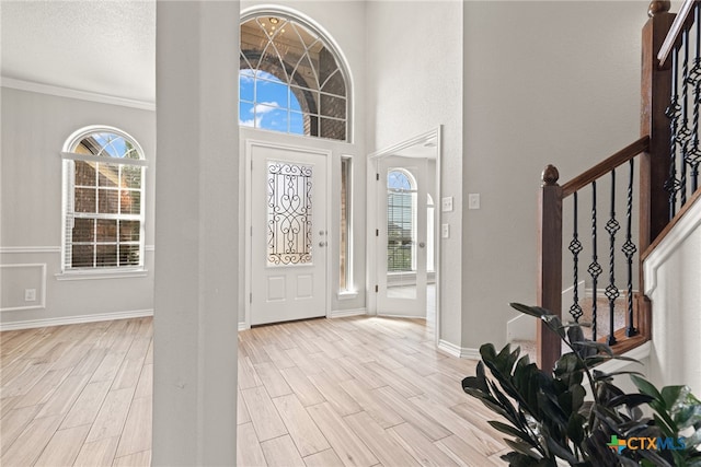 foyer entrance featuring light hardwood / wood-style floors, a towering ceiling, and crown molding