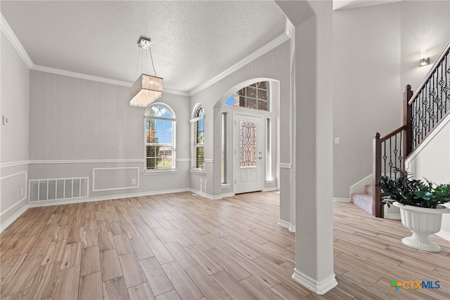 foyer entrance with a textured ceiling, light wood-type flooring, and ornamental molding