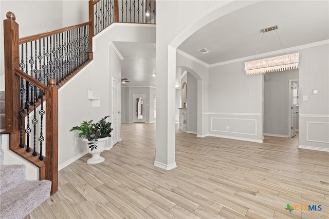 foyer featuring ornamental molding, light wood-type flooring, a towering ceiling, and an inviting chandelier