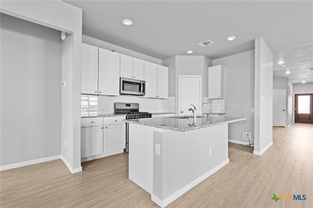 kitchen with light stone countertops, appliances with stainless steel finishes, a kitchen island with sink, sink, and white cabinetry