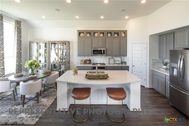 kitchen featuring a wealth of natural light, stainless steel appliances, gray cabinets, and a center island with sink