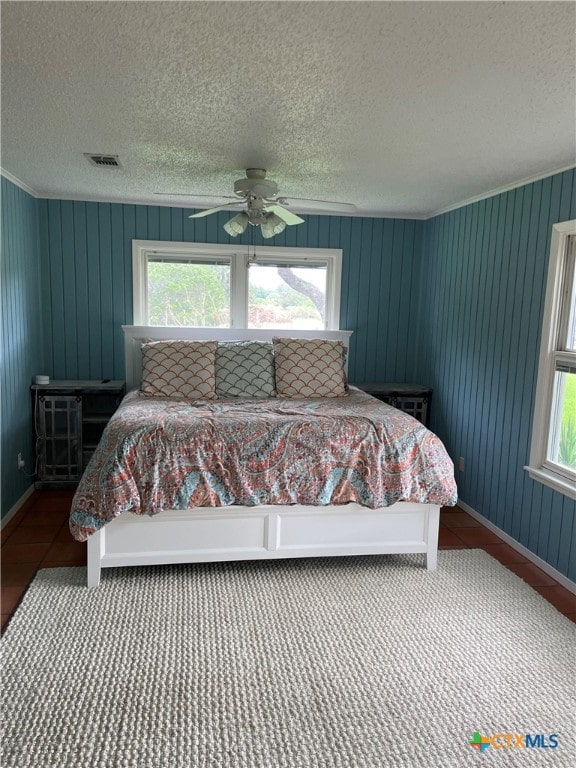 bedroom featuring ceiling fan, multiple windows, wooden walls, and a textured ceiling