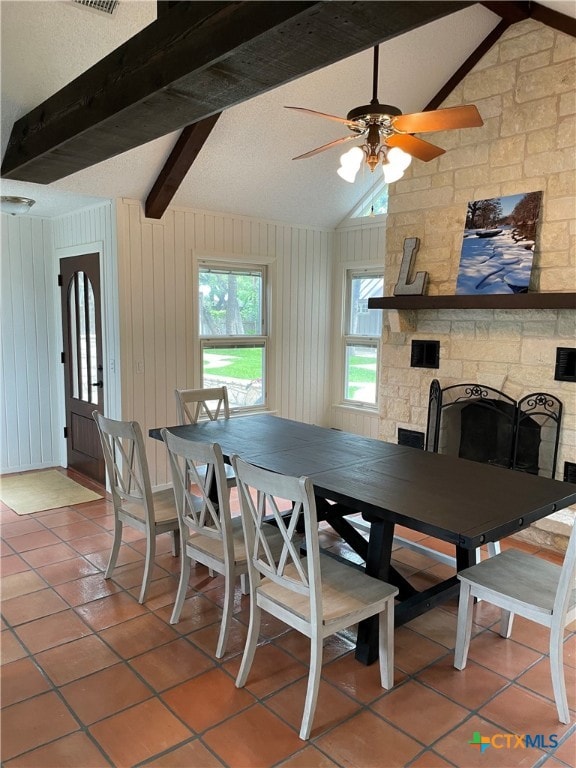 dining area with lofted ceiling with beams, a fireplace, wooden walls, tile patterned flooring, and ceiling fan