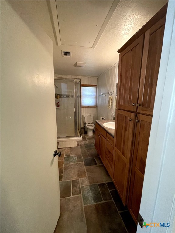 bathroom featuring a shower with door, vanity, toilet, and a textured ceiling