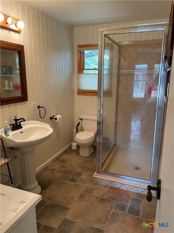 bathroom with toilet, wood walls, a textured ceiling, and a shower with shower door