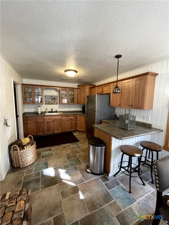 kitchen with a breakfast bar area, a textured ceiling, decorative light fixtures, and kitchen peninsula