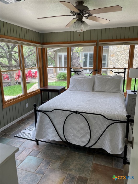 bedroom with a textured ceiling, wood walls, multiple windows, and ceiling fan