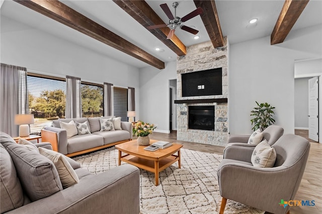 living room with light wood-type flooring, ceiling fan, a stone fireplace, and beam ceiling