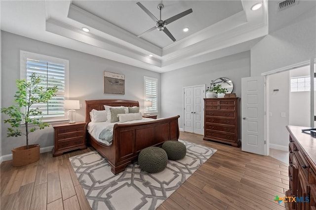 bedroom with baseboards, a tray ceiling, light wood-type flooring, and visible vents