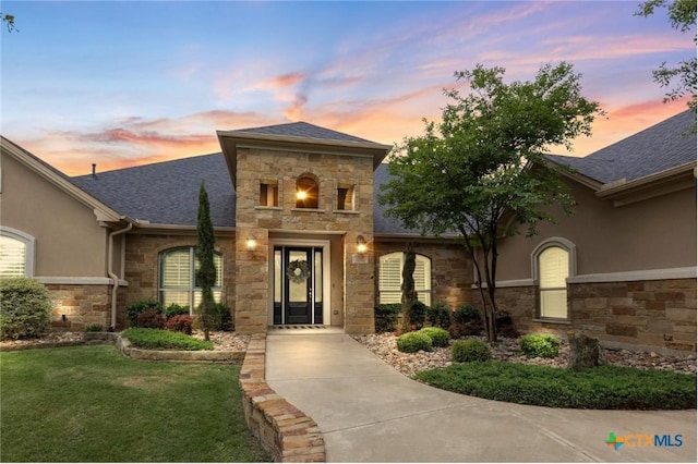 doorway to property featuring a shingled roof, stucco siding, and stone siding