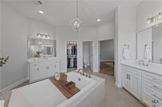 full bathroom featuring an inviting chandelier, a sink, two vanities, visible vents, and a bath