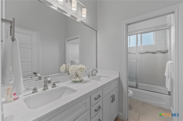 bathroom featuring double vanity, a sink, enclosed tub / shower combo, and toilet