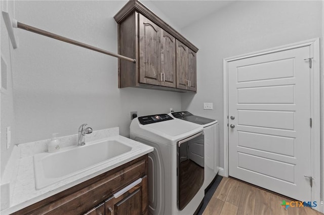 laundry room with a sink, cabinet space, light wood-style flooring, and washing machine and clothes dryer