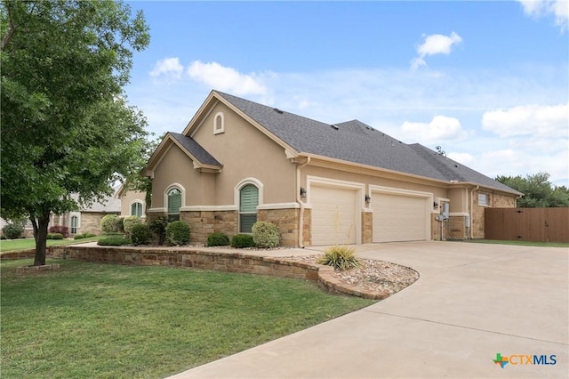 view of front facade with driveway, a front yard, an attached garage, stone siding, and stucco siding