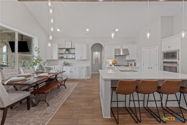 kitchen with white cabinets, a sink, arched walkways, stainless steel appliances, and under cabinet range hood